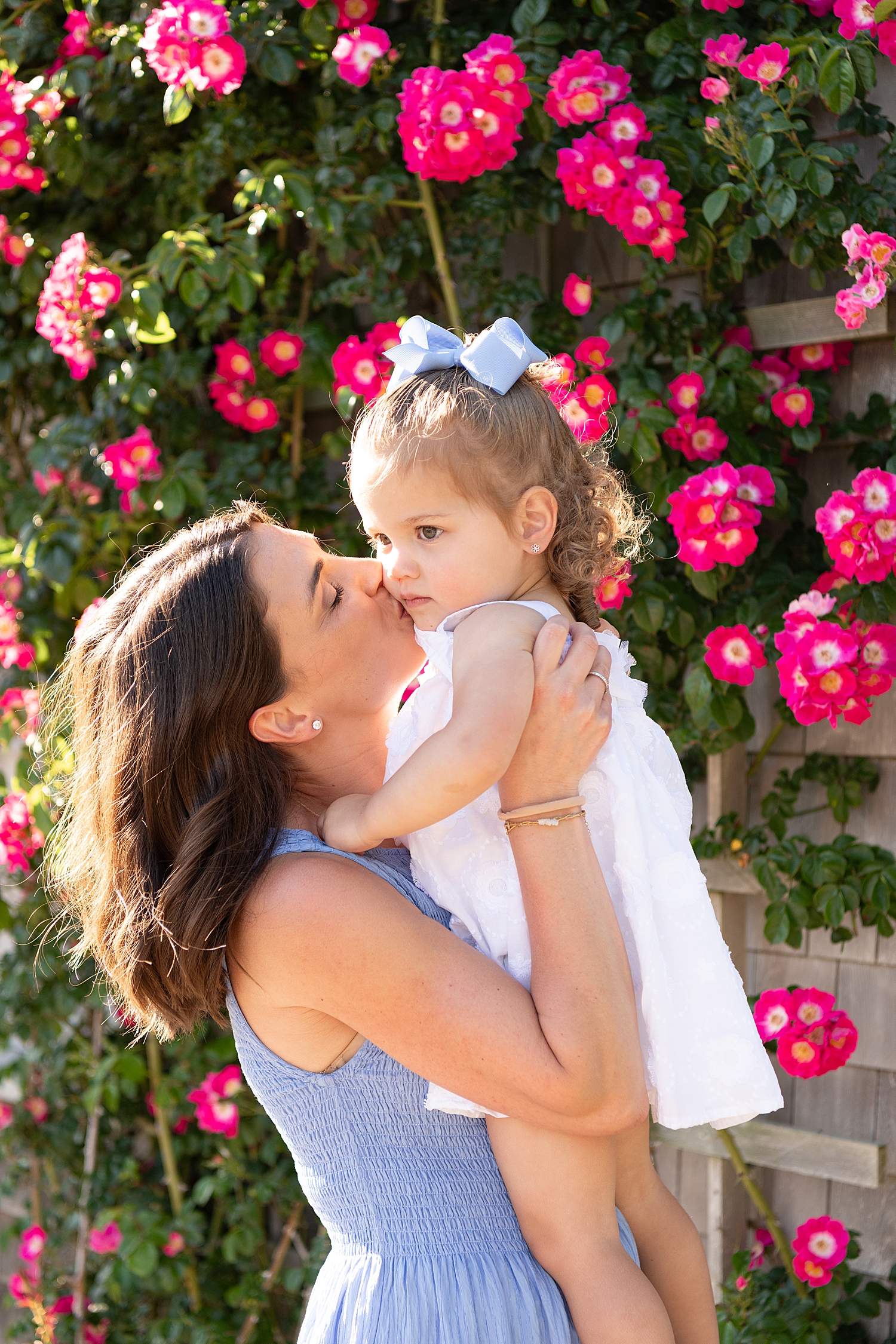 mother kisses daughter in front of red flowers by Massachusetts photographer