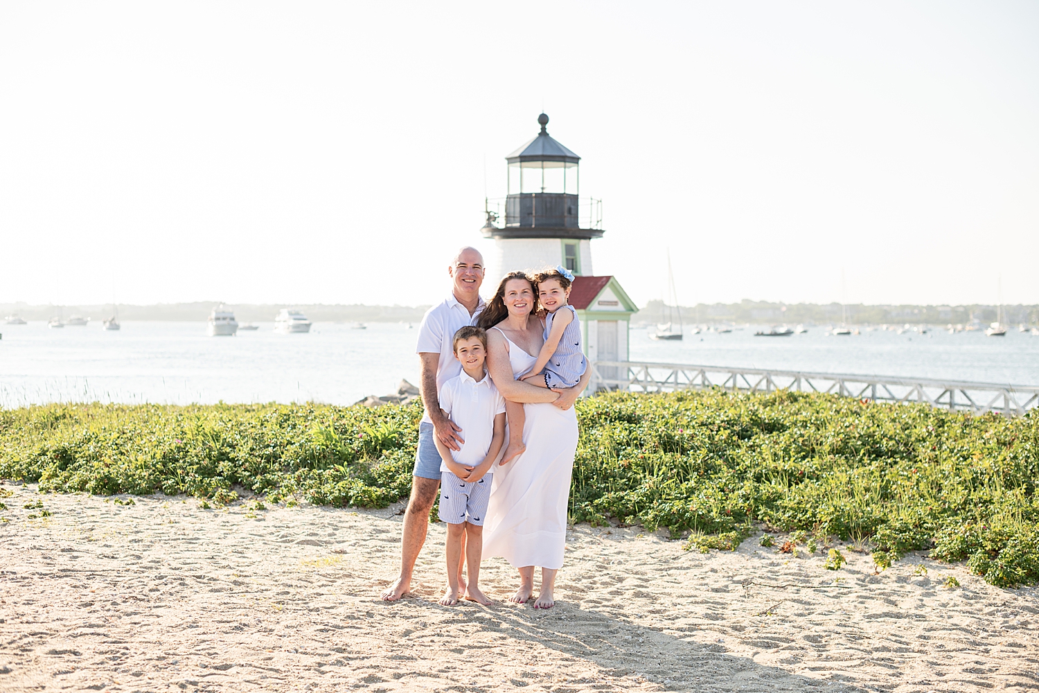 family of four stands in front of lighthouse at golden hour by Nantucket photographer