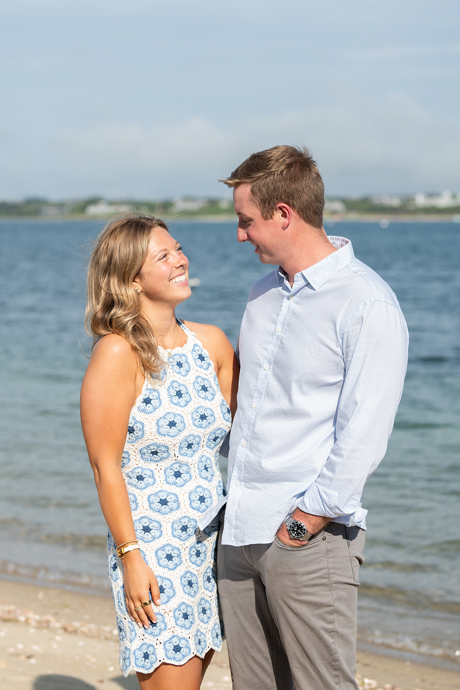 couple grins at each other in front of water for proposal at Brant Point Lighthouse
