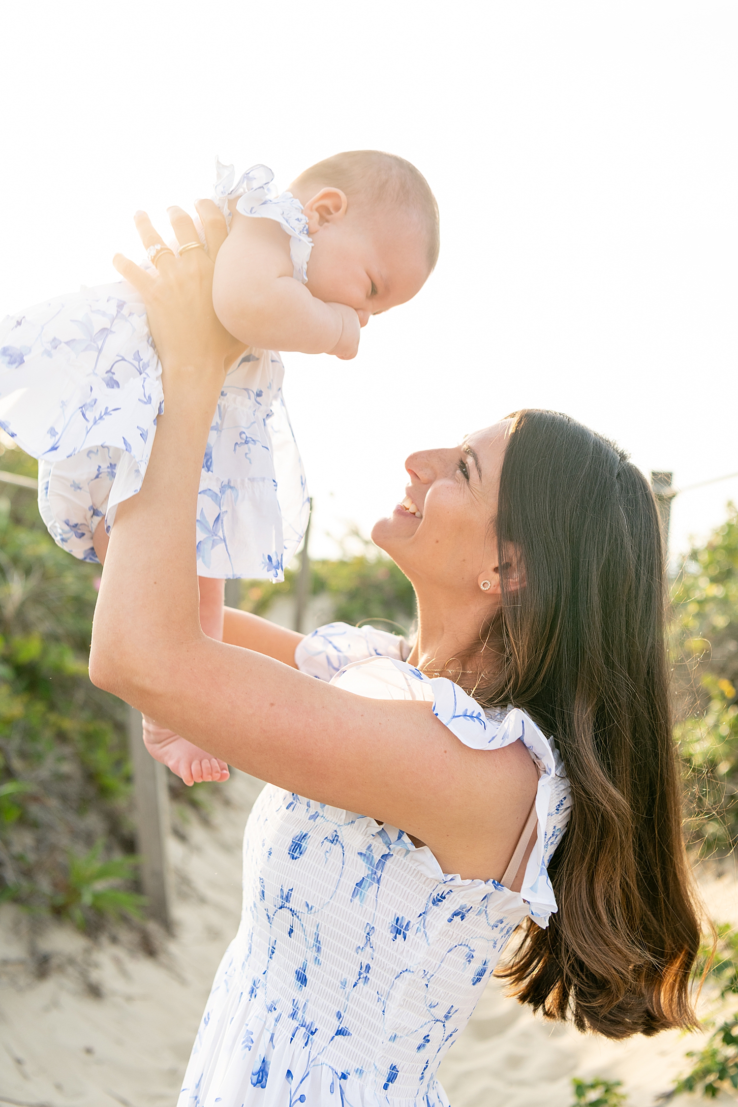 mother in blue and white dress lifts up her six month old daughter for extended family session