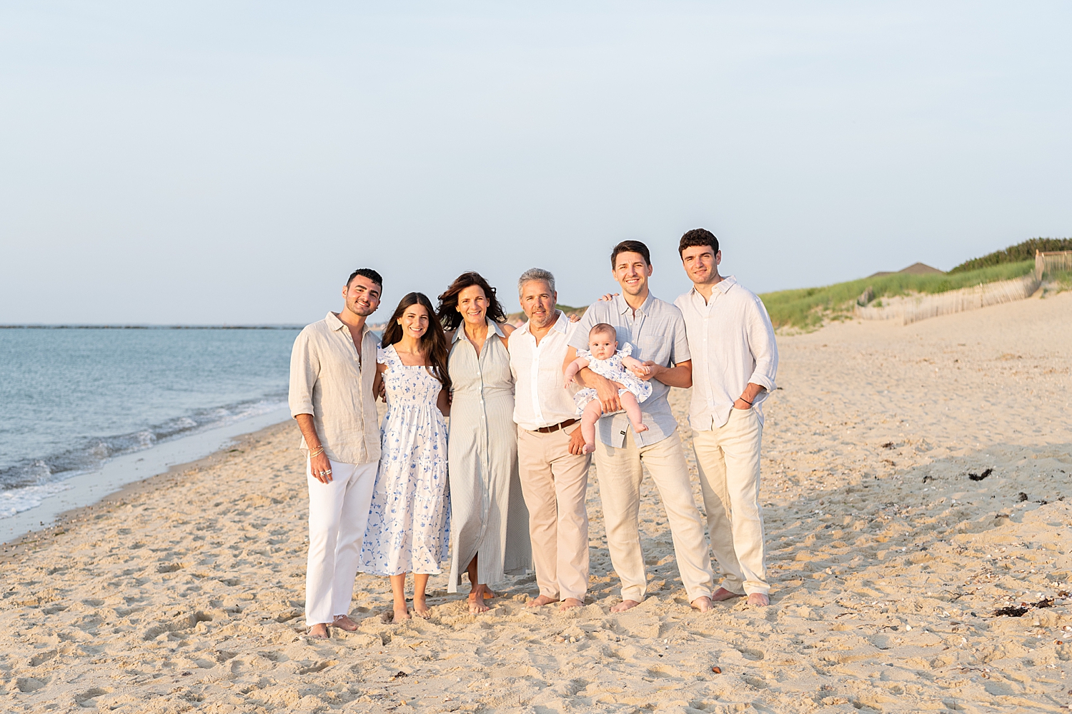 grandparents stand with sons and daughters and grandbaby on the sand by Nantucket photographer
