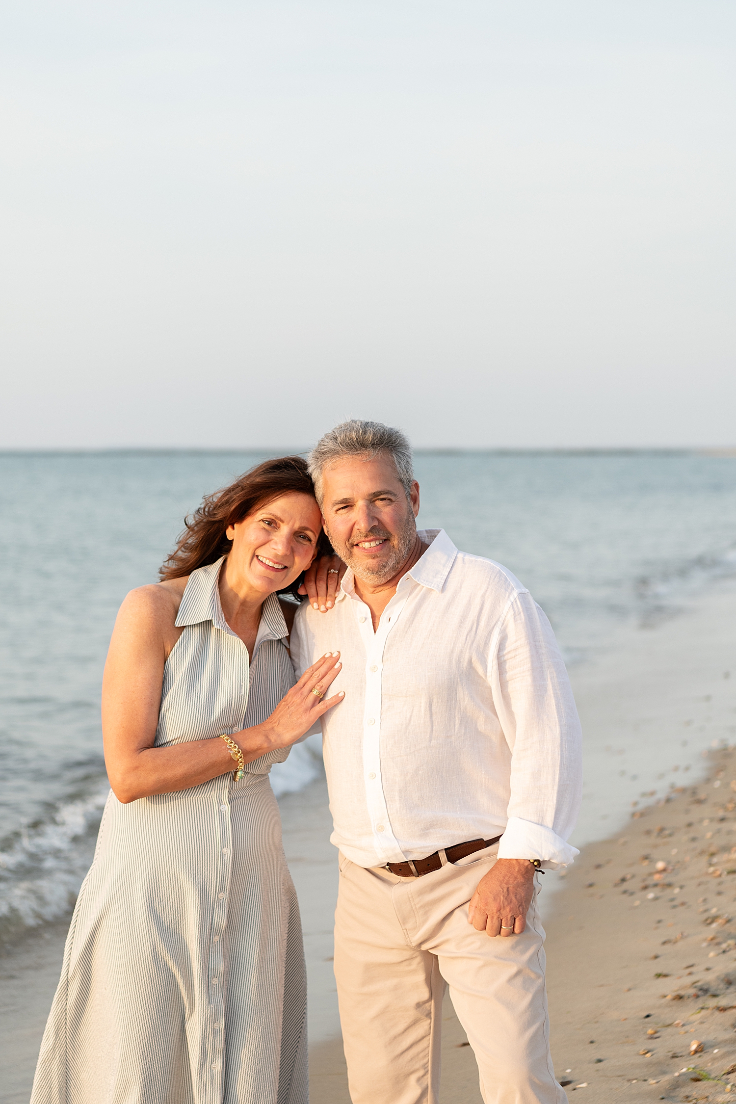 grandparents stand next to the ocean hugging for extended family session