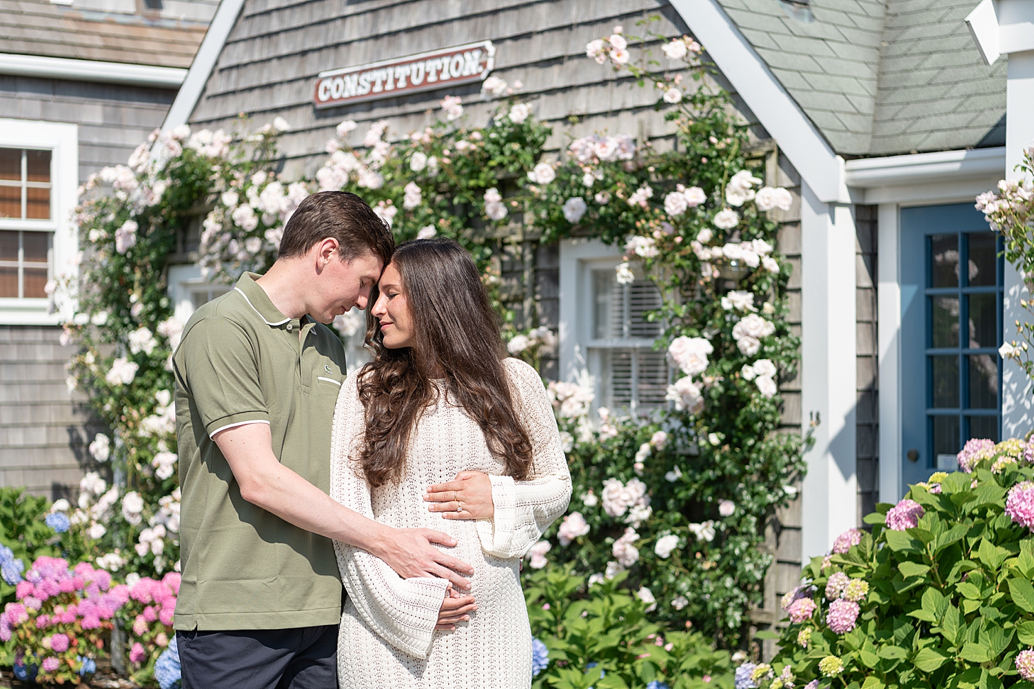 couple embrace and hold pregnant belly in front of flowers by Nantucket photographer