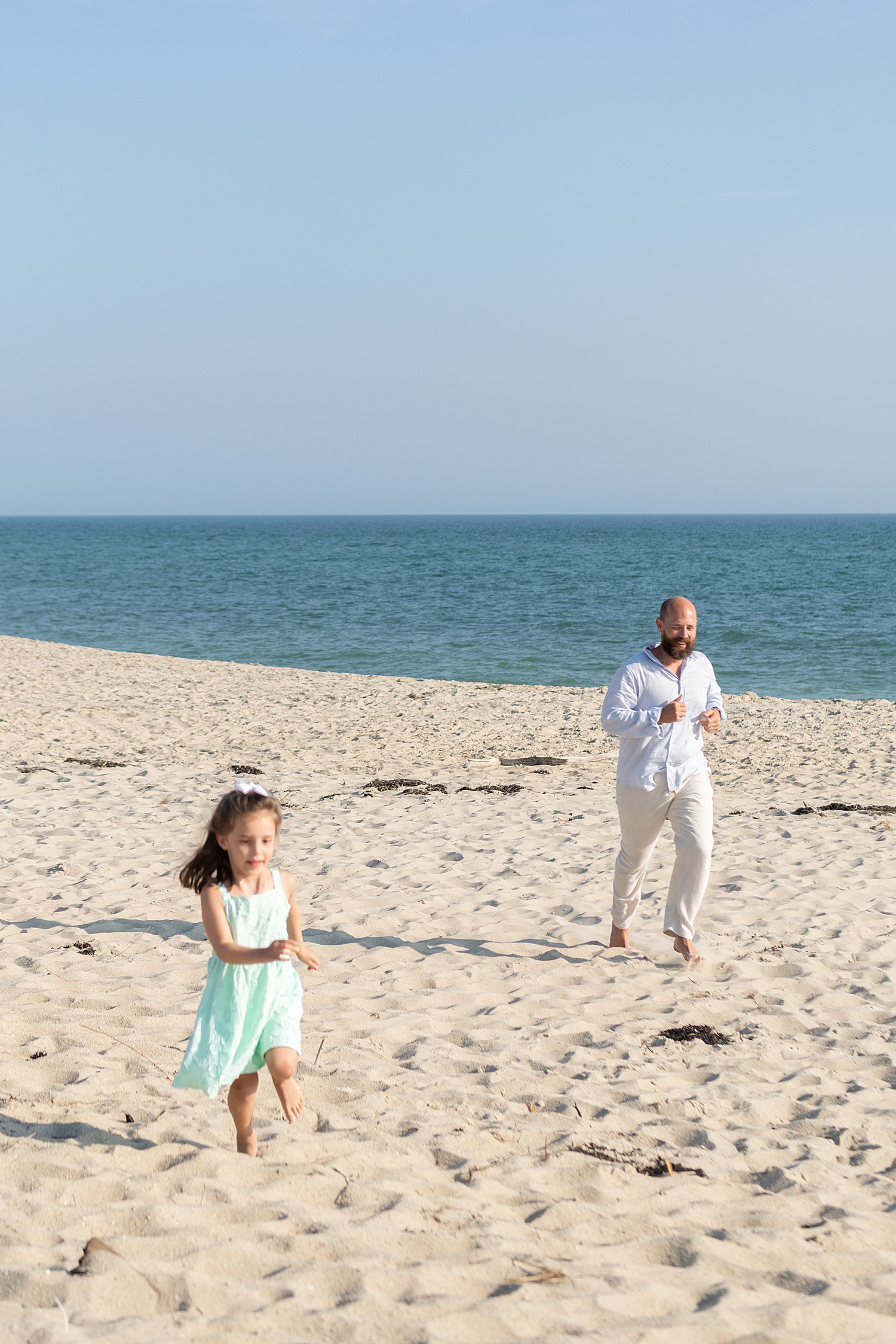 dad and daughter run together on the beach for family session on your vacation