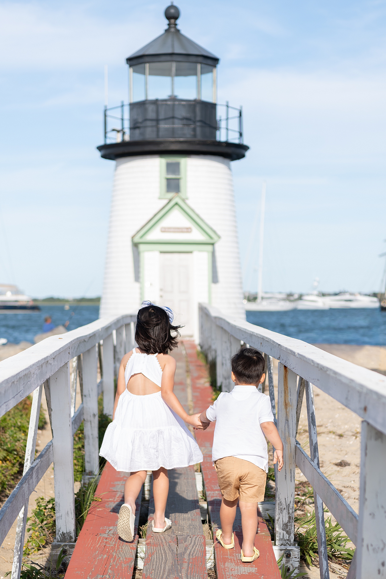 two kids walk hand in hand up to a lighthouse by Nantucket photographer