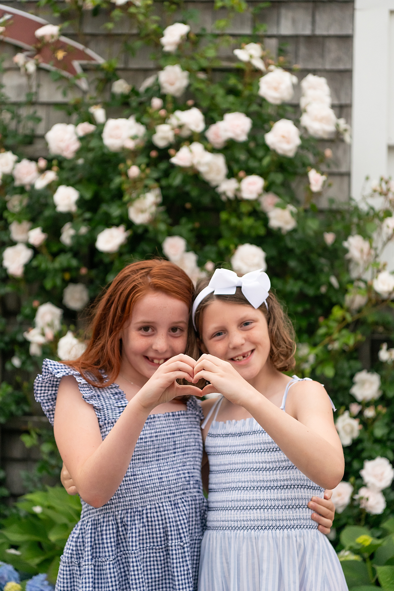 two cousins hold up heart hands in front of roses by Rachel Elizabeth Photography