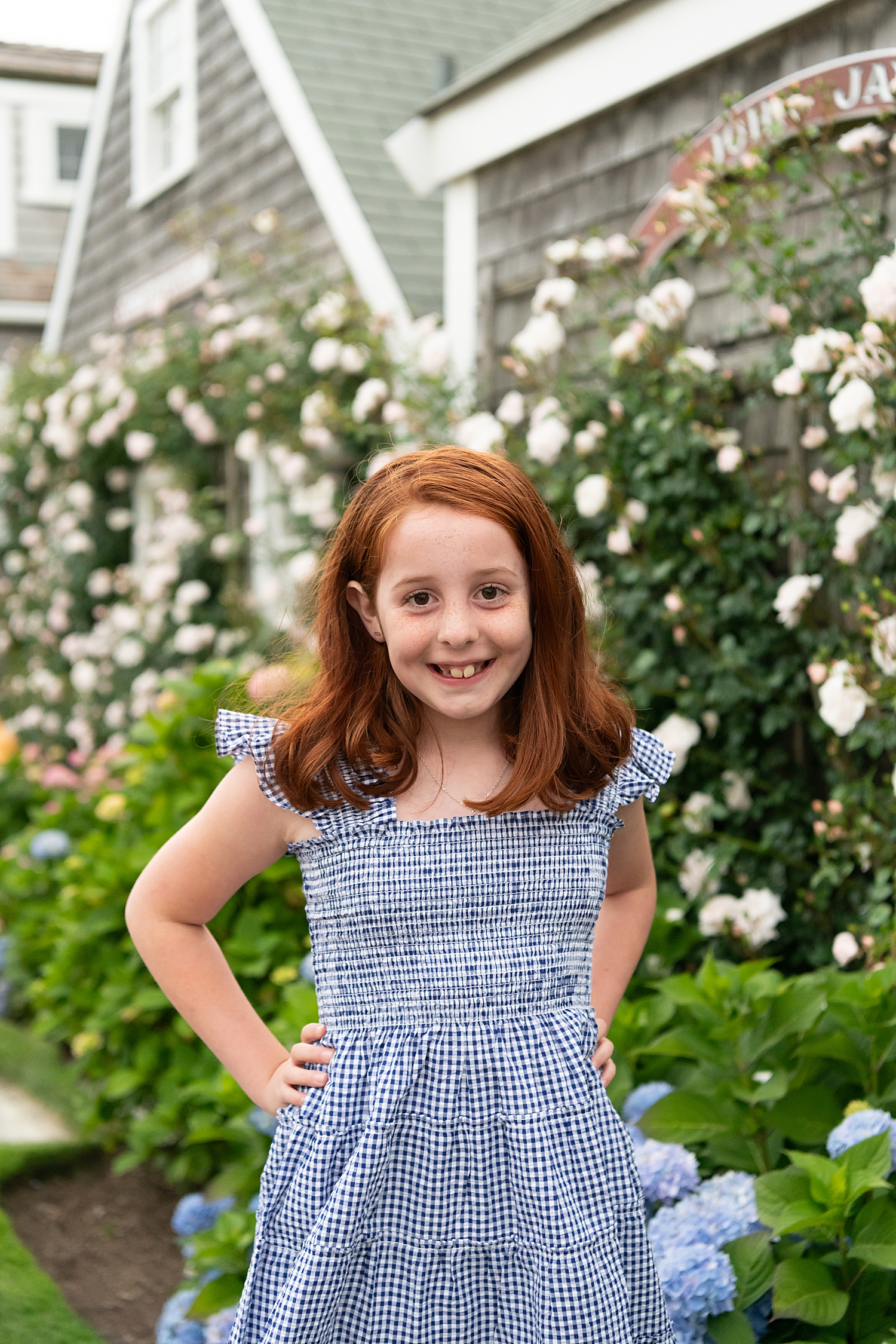 redhead girl in blue dress stands in front of roses by Rachel Elizabeth Photography