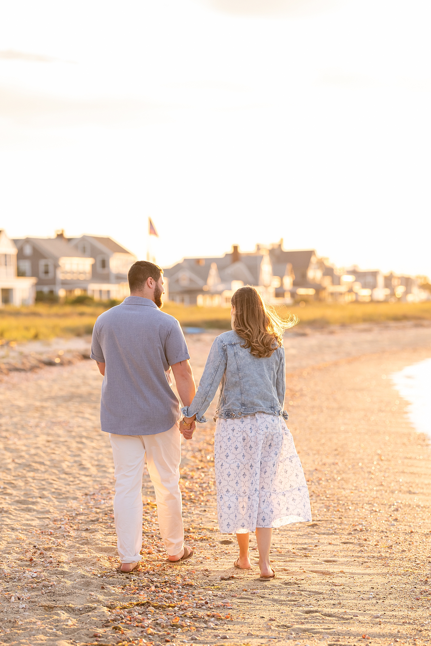 man and woman walk hand in hand down beach for Sunset Proposal at Brant Point Lighthouse