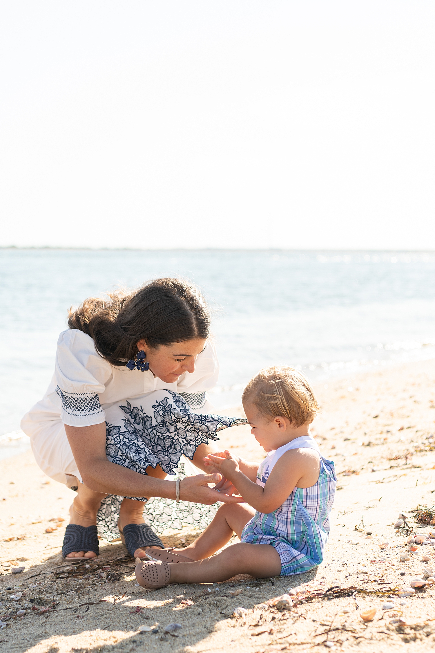 brunette mother kneels in sand with her baby by Nantucket Portrait Photographer