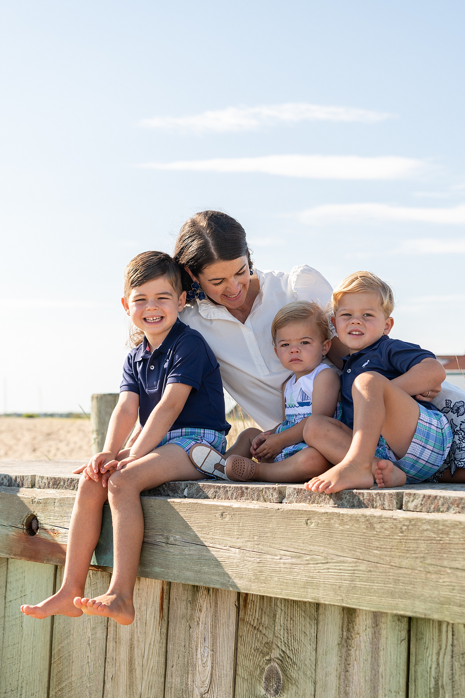 mother sits with three boys on beach wall for family of five session