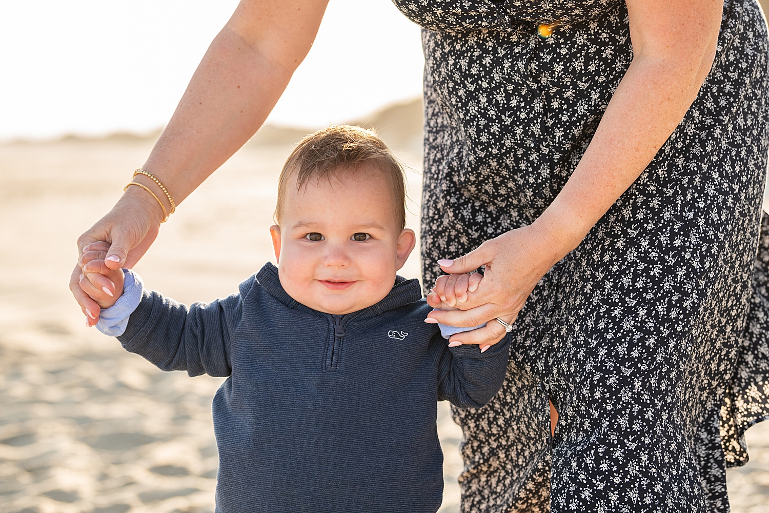 small toddler holds his moms hands on the beach showing what time of day is best for family photos