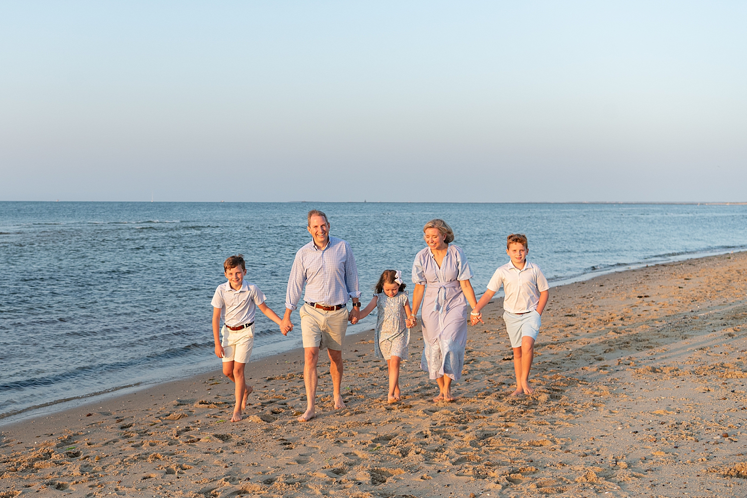 mom and dad walk with kids on beach during sunset showing what time of day is best for family photos
