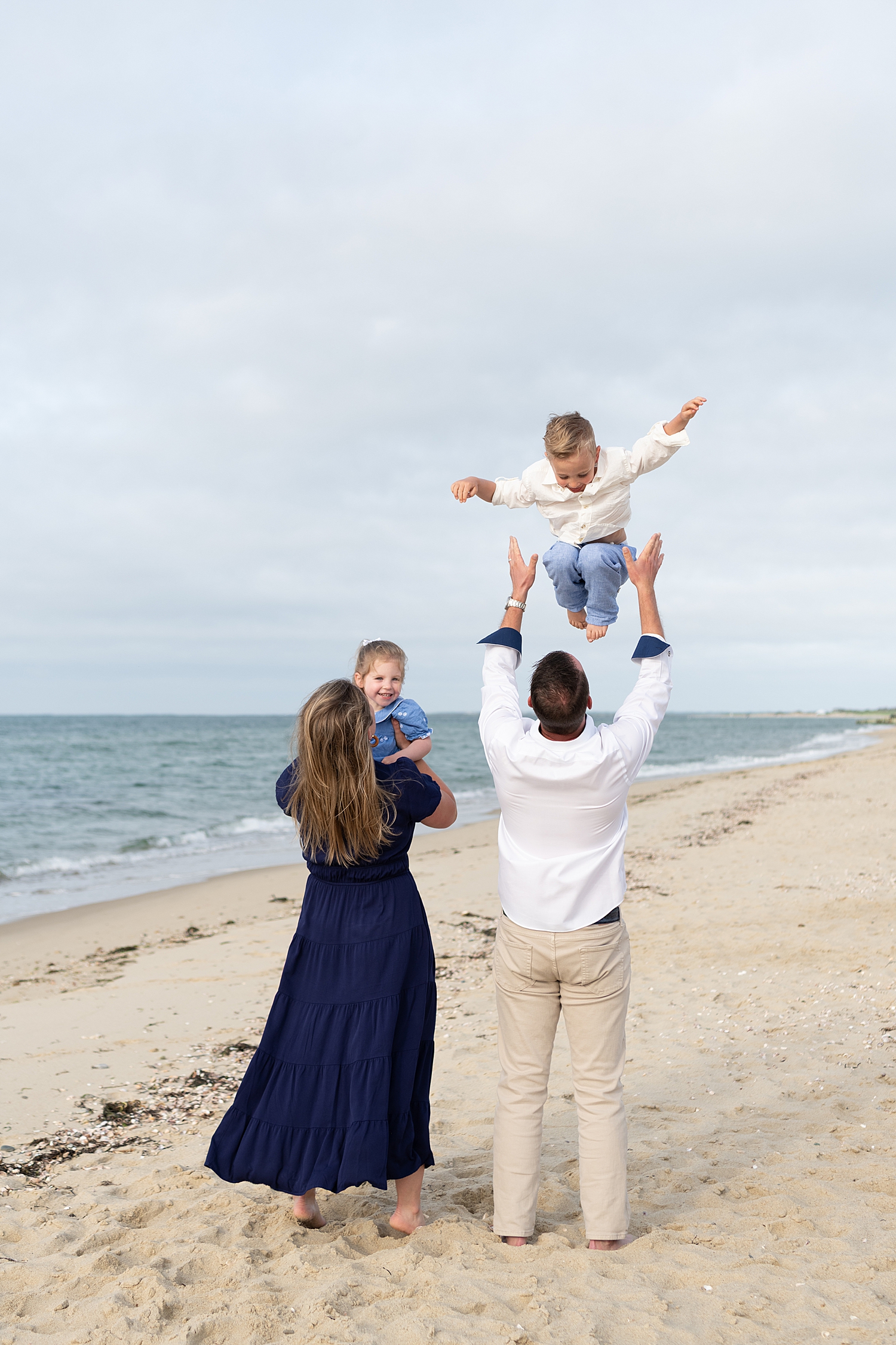 dad throws up his son in the air next to water by Rachel Elizabeth Photography