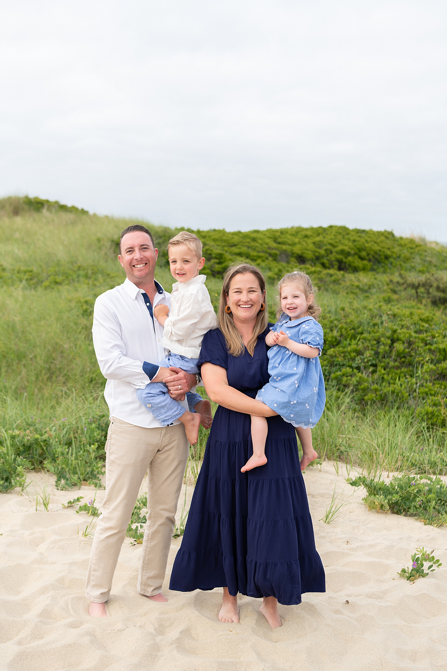 family of four stand in front of sand hill by Nantucket Family Photographer