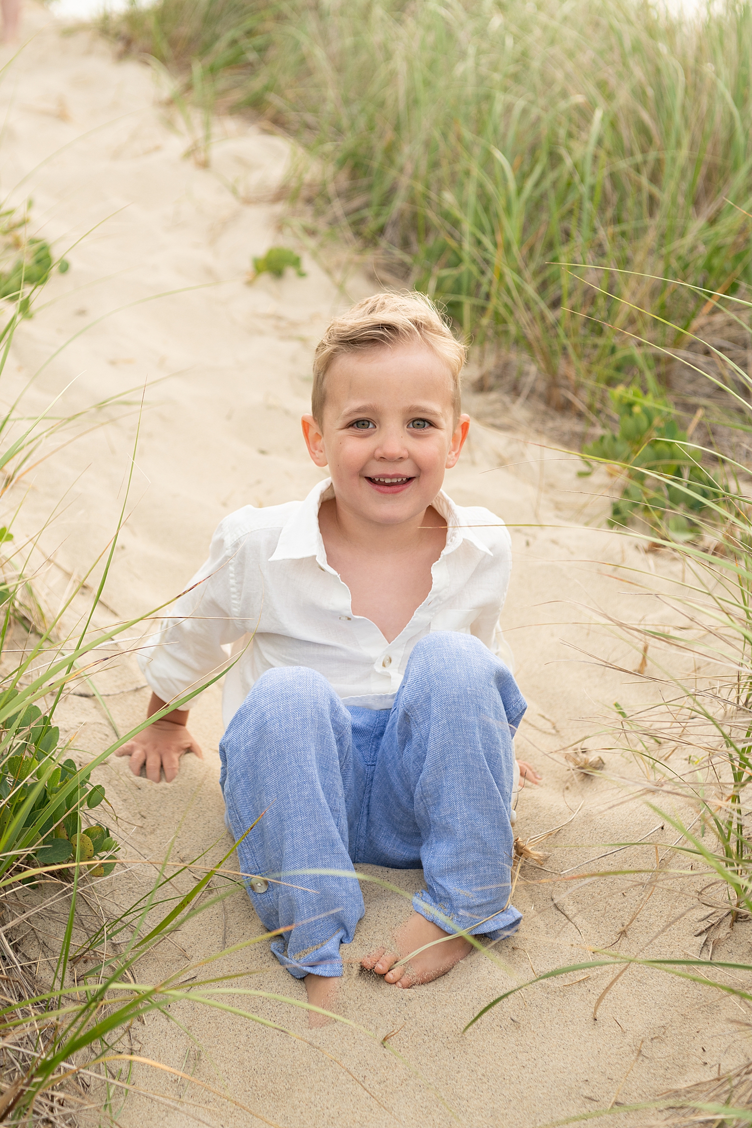 blonde kid sits in the sand next to grass by Rachel Elizabeth Photography