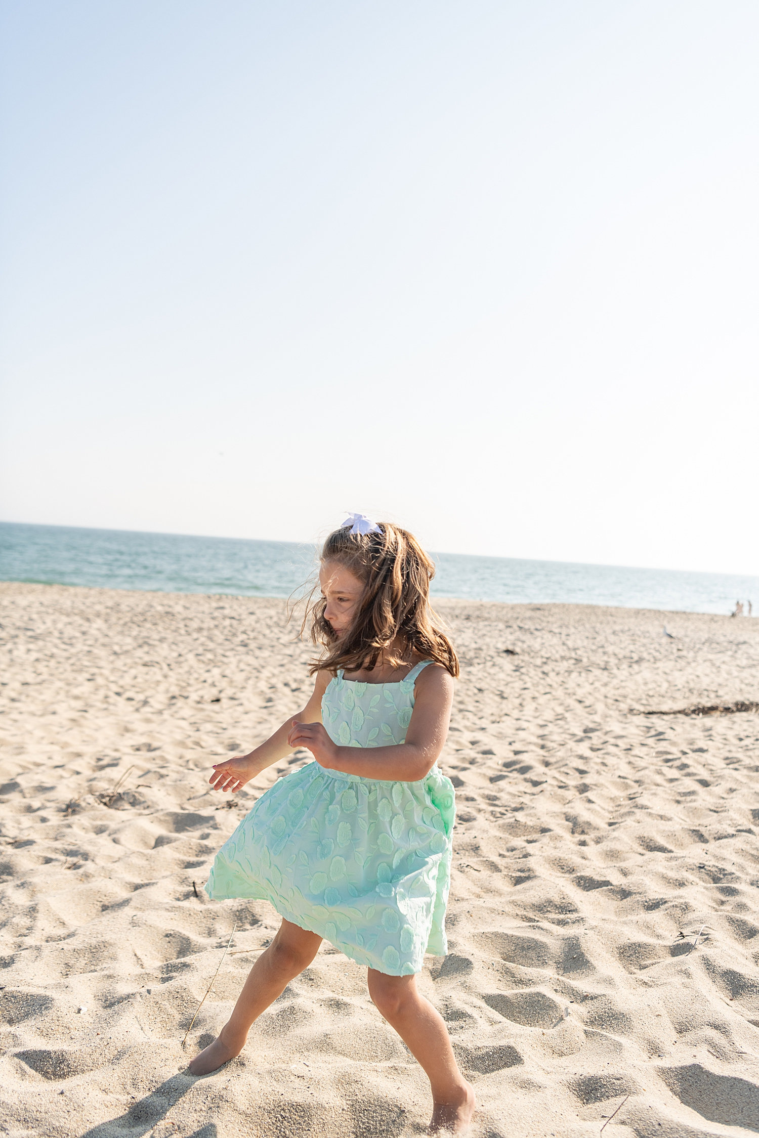 little girl in teal dress dances by the ocean by Nantucket vacation photographer