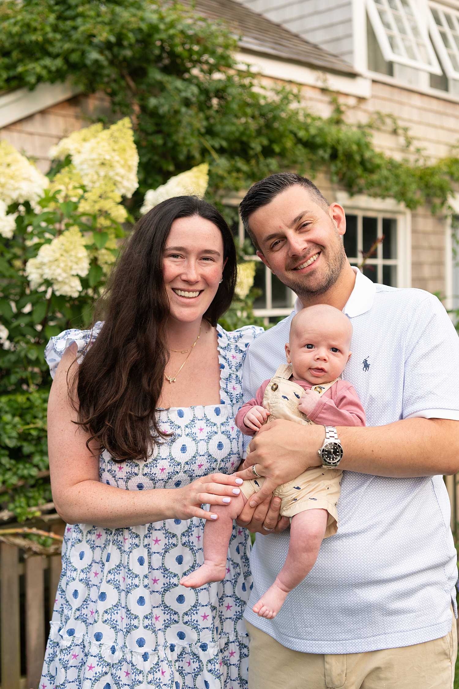 parents hold their small baby in front of hydrangeas in a Nantucket location