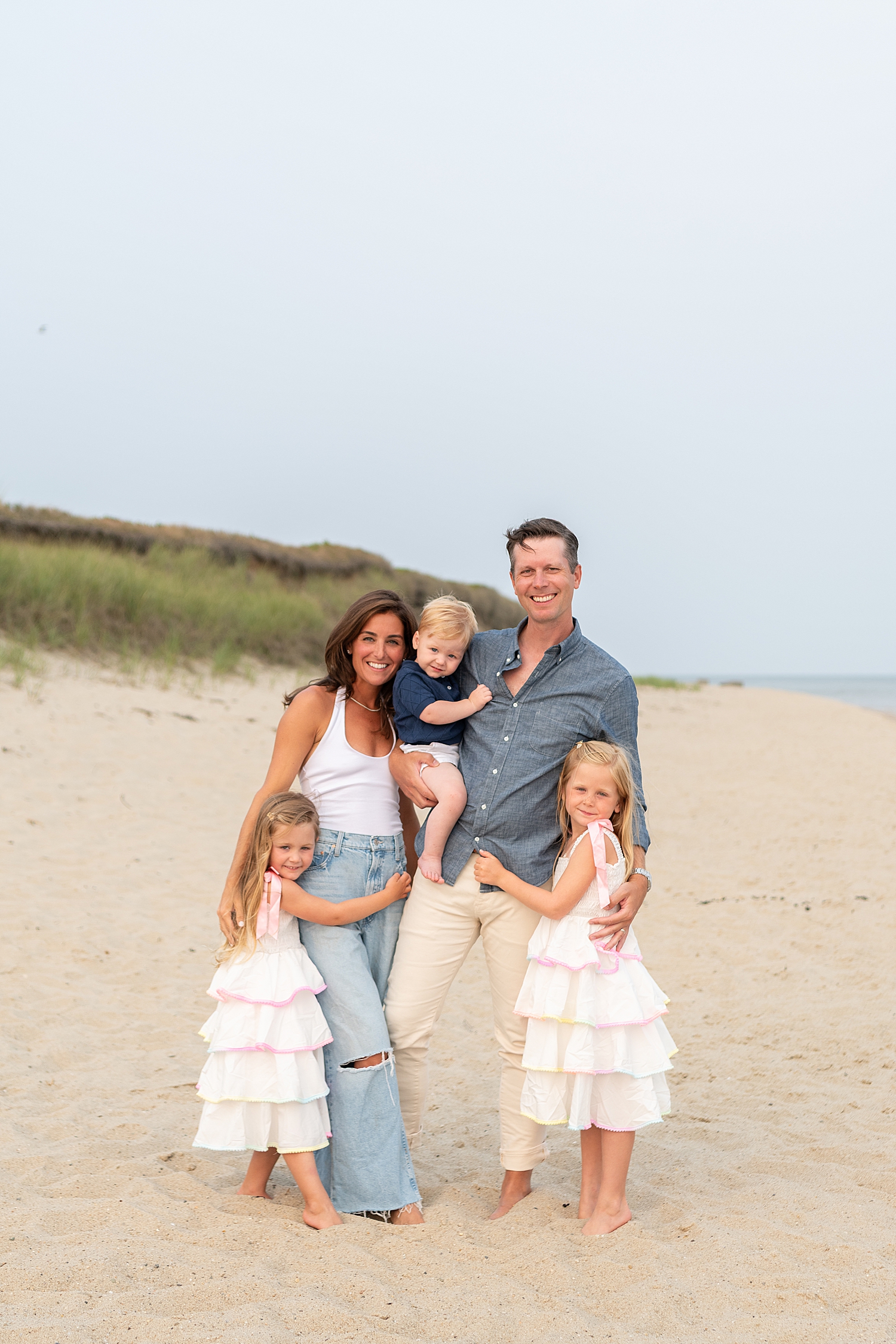 mom and dad with three small children stand together by Nantucket family photographer