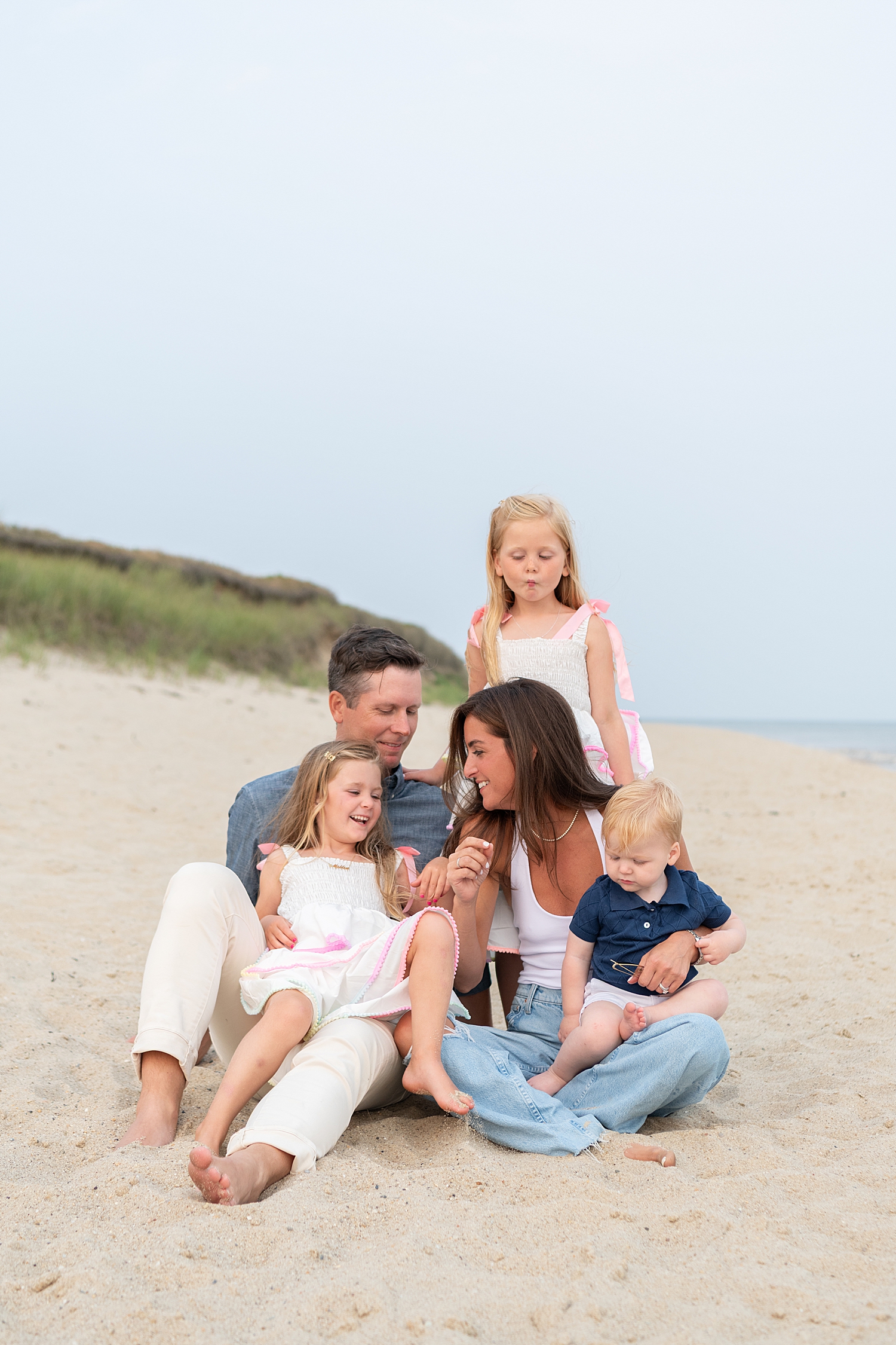 parents sit by sand dune with three kids by Nantucket family photographer