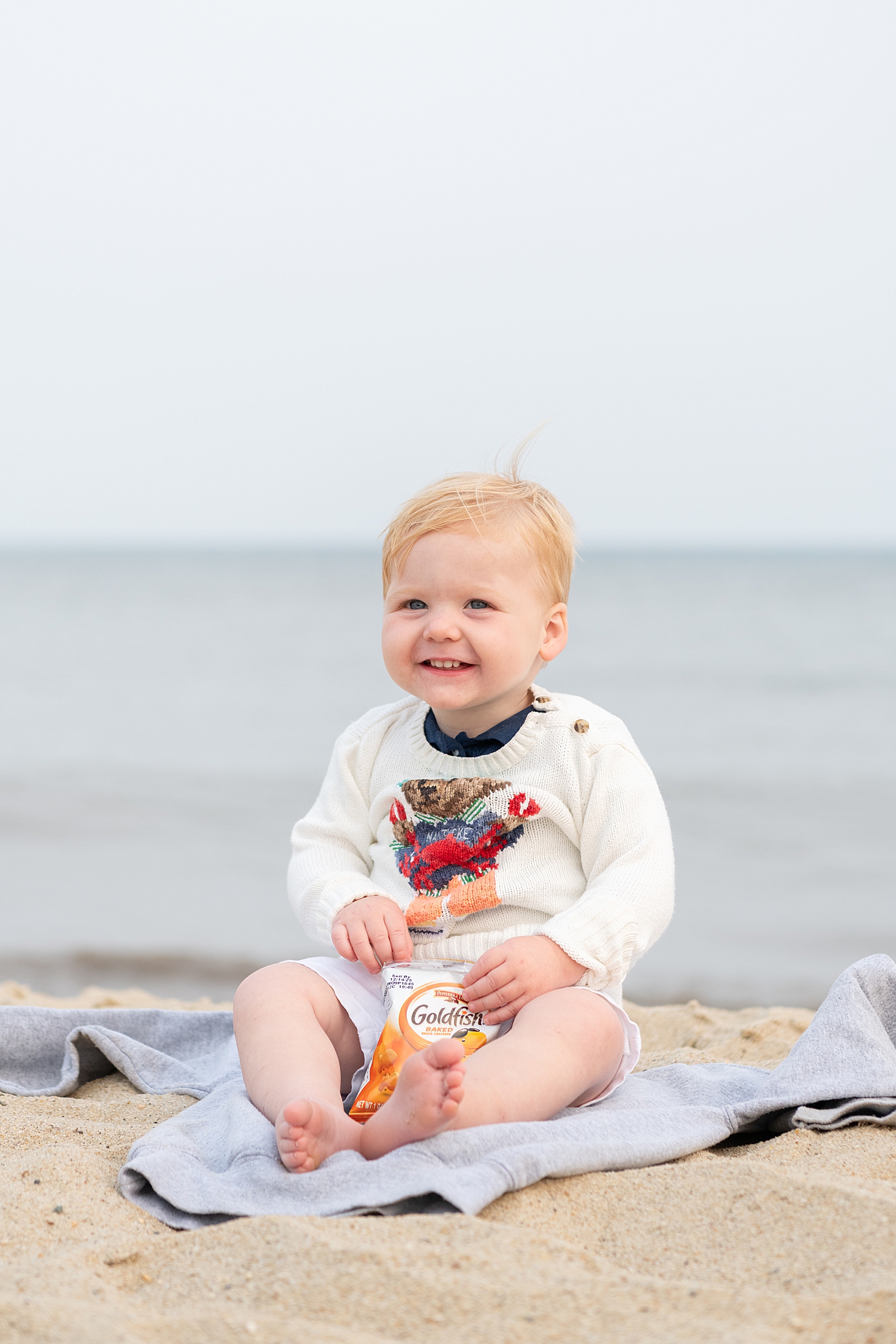 one year old sits on jacket on the sand by Nantucket family photographer