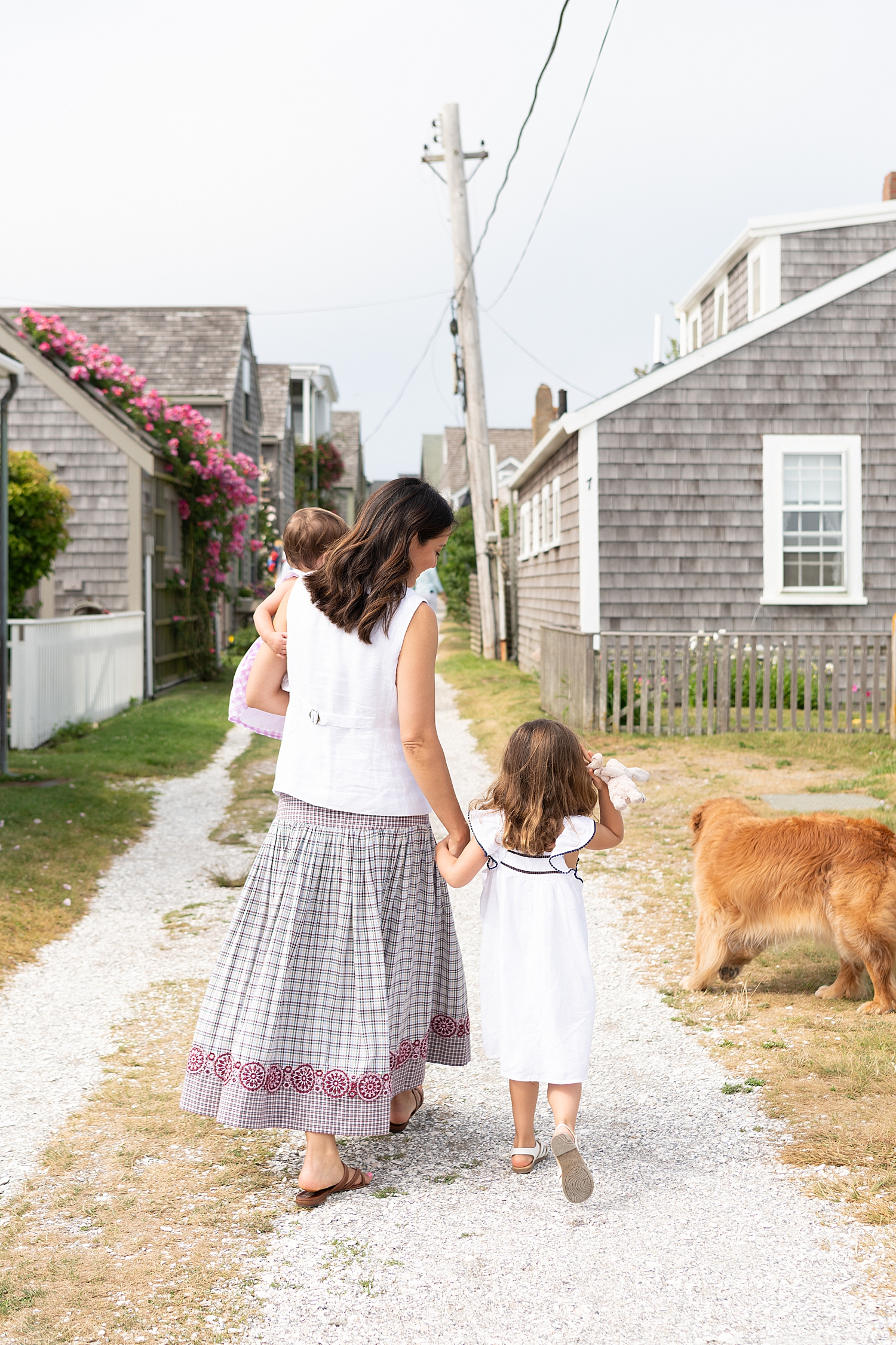 mother in skirt walks gravel path with her small children by Nantucket family photographer
