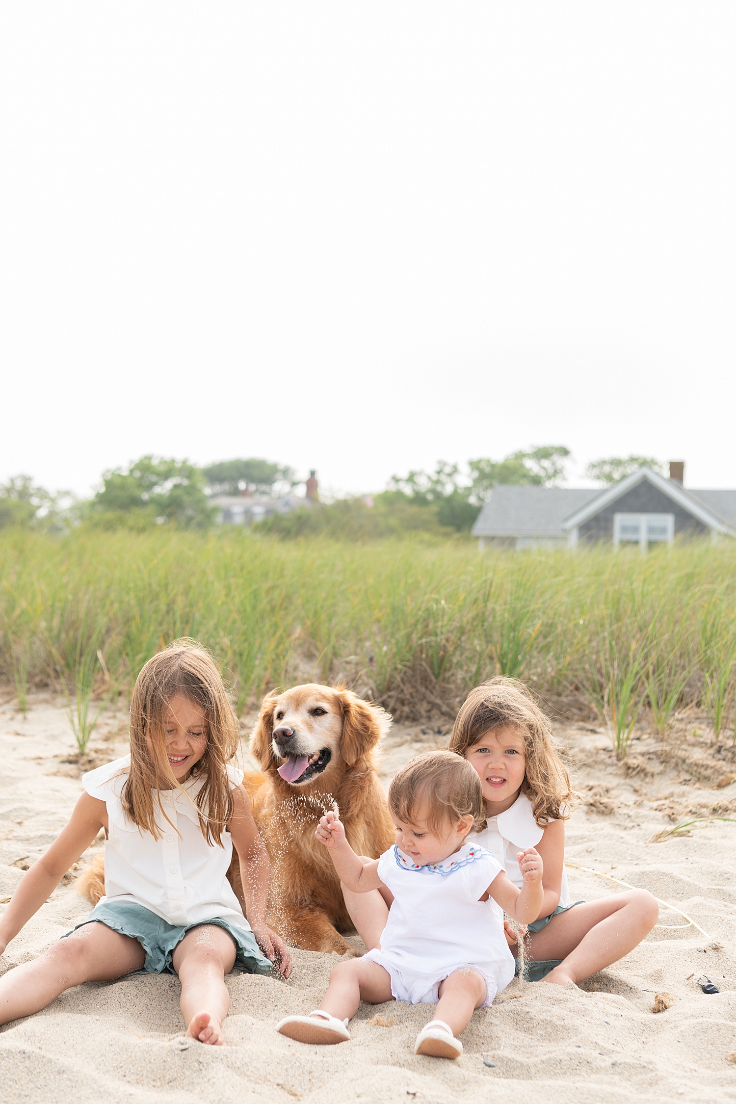 three small children around their dog on the sand by Nantucket family photographer
