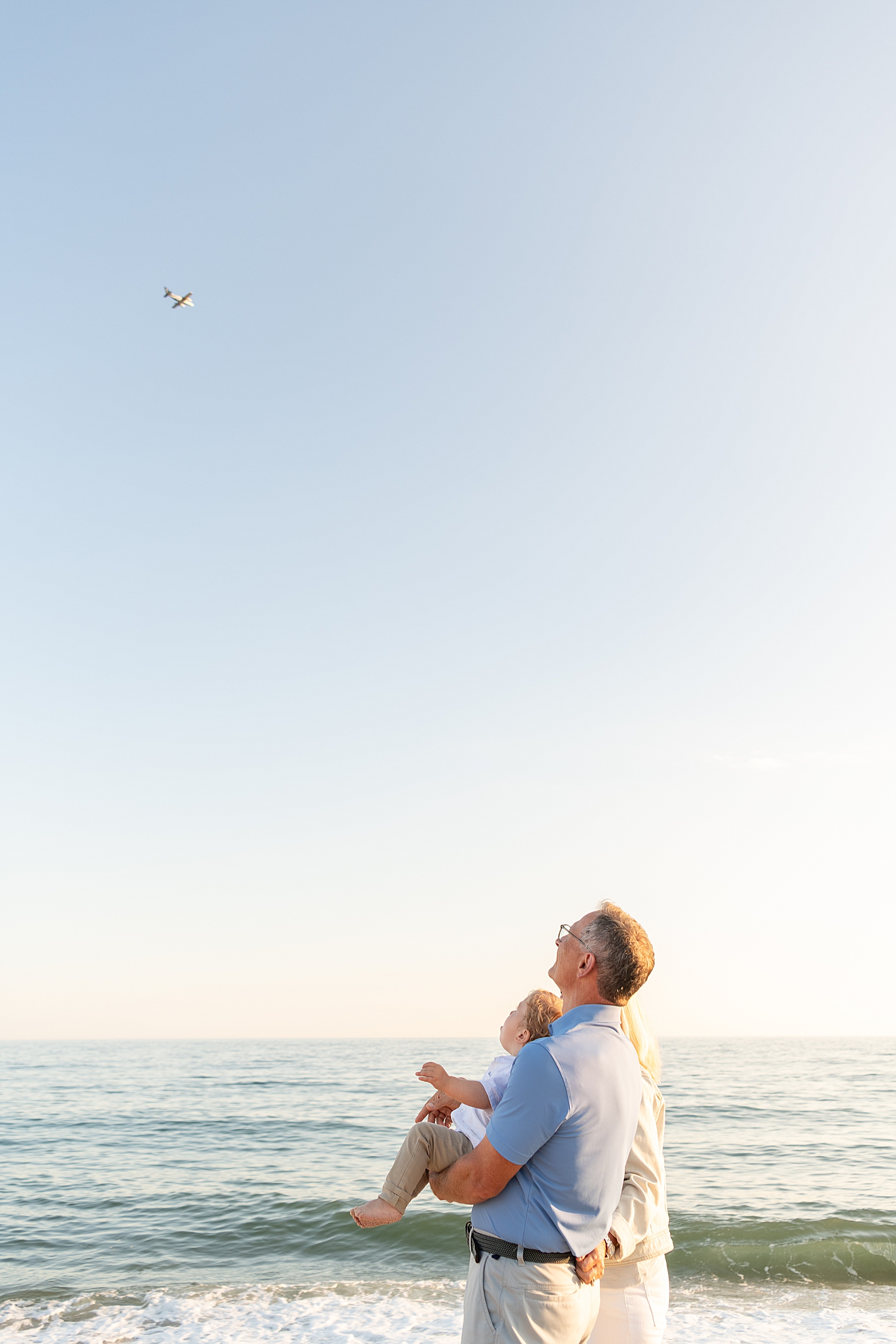 grandparents watch plane in sky with toddler by ocean by Nantucket family photographer
